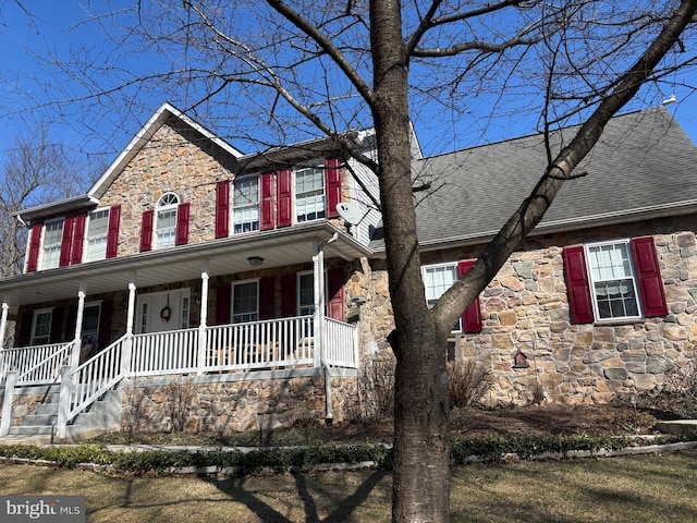 colonial home featuring stone siding, a porch, and roof with shingles