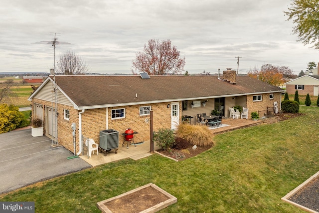 back of house with a patio, a garage, central air condition unit, a lawn, and brick siding