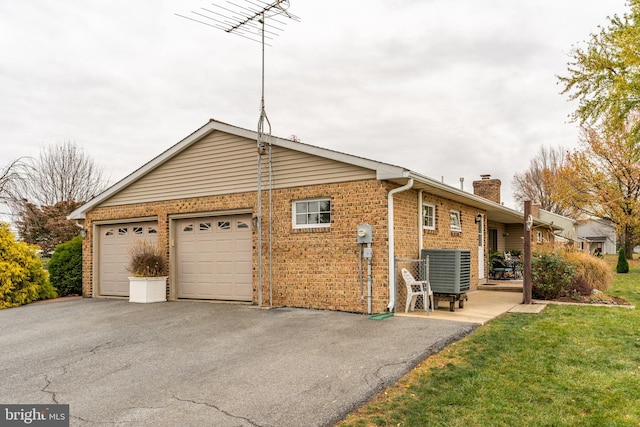 view of side of property with a yard, cooling unit, a garage, brick siding, and a chimney