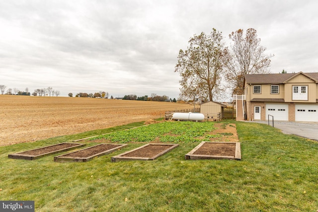 view of yard with an outdoor structure, a garden, an attached garage, and a rural view