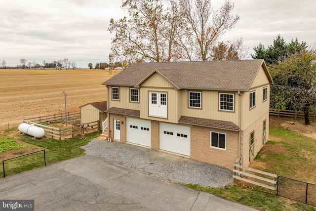 view of front facade with a rural view, a shingled roof, and fence