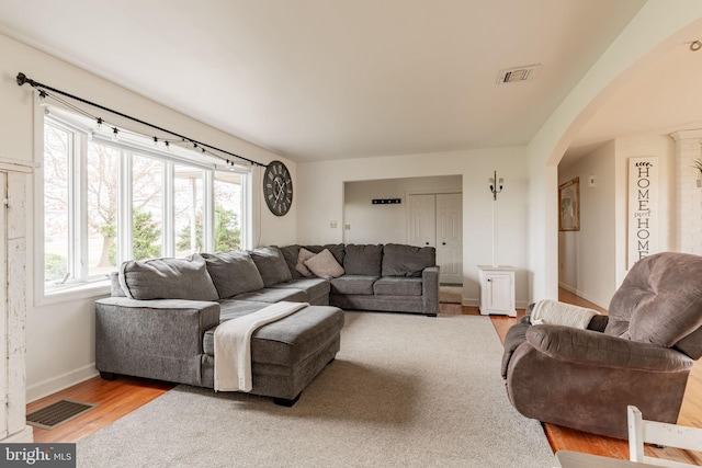 living area with light wood finished floors, visible vents, arched walkways, and baseboards