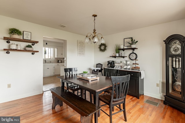 dining space featuring visible vents, baseboards, light wood-type flooring, and an inviting chandelier