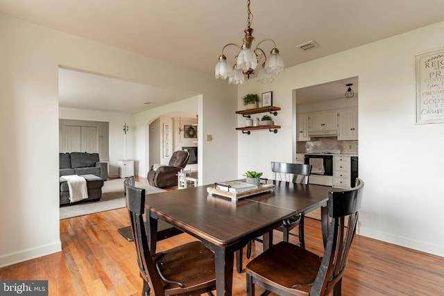 dining room with visible vents, baseboards, light wood-type flooring, an inviting chandelier, and arched walkways