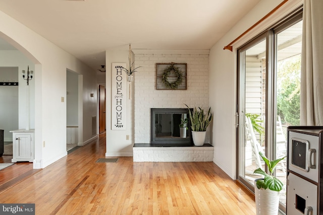 unfurnished living room with light wood finished floors, a brick fireplace, baseboards, and arched walkways