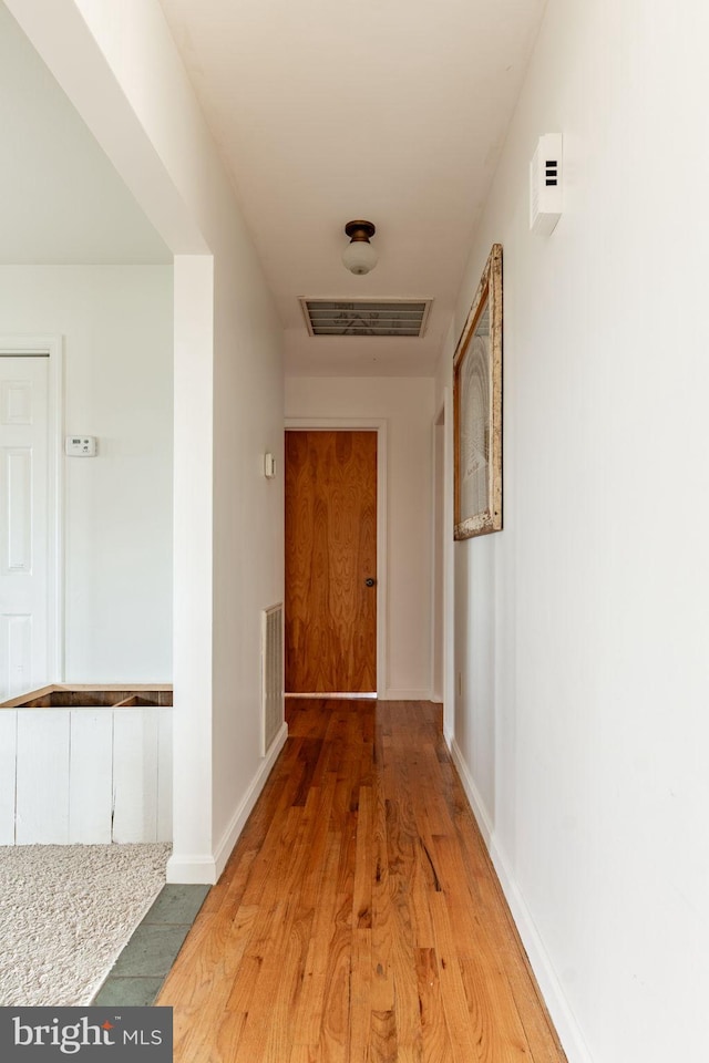 corridor with light wood-style floors, visible vents, and baseboards