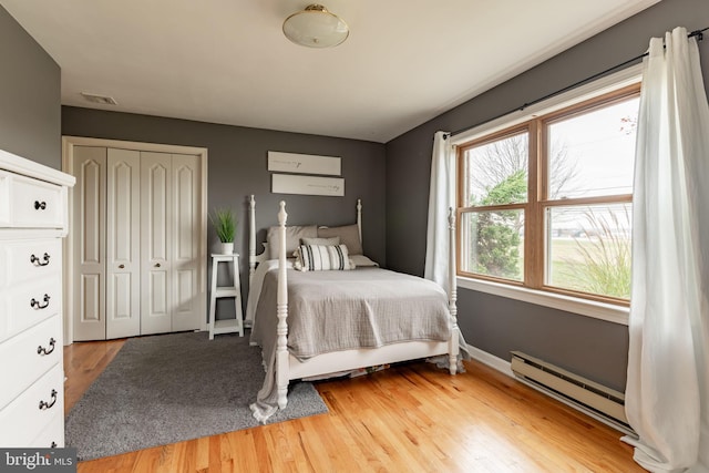 bedroom with visible vents, baseboards, baseboard heating, light wood-style floors, and a closet