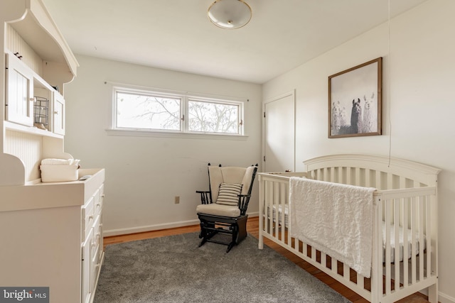 bedroom featuring a crib, wood finished floors, and baseboards