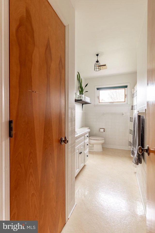 bathroom with toilet, tile walls, wainscoting, and vanity