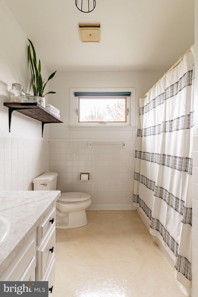 bathroom with vanity, a shower with shower curtain, wainscoting, tile walls, and toilet