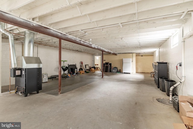 unfinished below grade area featuring concrete block wall and freestanding refrigerator