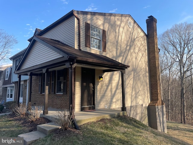 view of front of house with brick siding, a porch, and a chimney