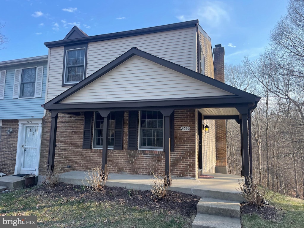 view of front of home with covered porch, brick siding, and a chimney