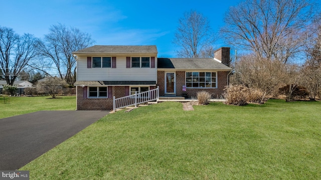 tri-level home featuring brick siding, a chimney, aphalt driveway, and a front yard