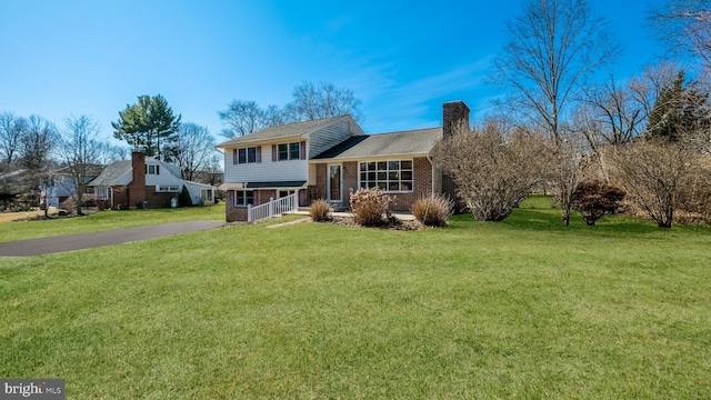 split level home with aphalt driveway, brick siding, a front yard, and a chimney