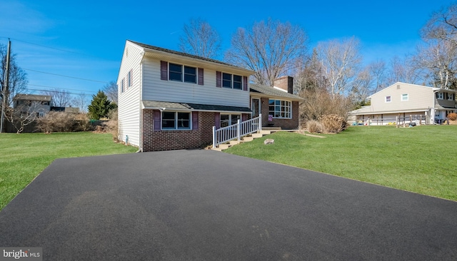 split level home featuring a front lawn, aphalt driveway, brick siding, and a chimney