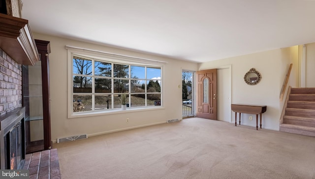 unfurnished living room with visible vents, carpet, stairs, and a fireplace with flush hearth