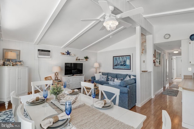 living room with a ceiling fan, an AC wall unit, vaulted ceiling with beams, and light wood-style floors