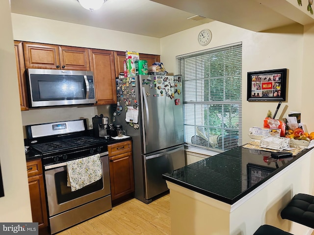 kitchen with dark countertops, brown cabinetry, light wood-style floors, and appliances with stainless steel finishes