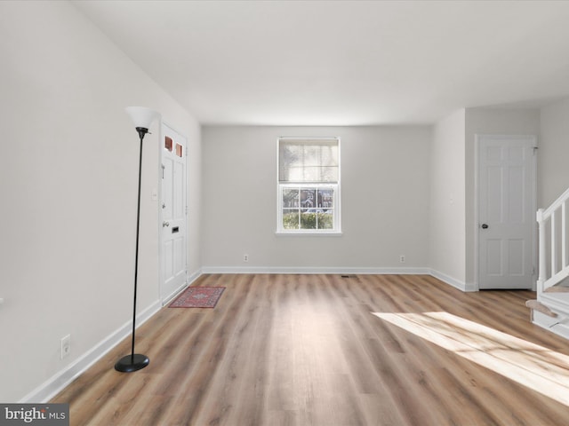 spare room featuring light wood-type flooring, stairs, and baseboards