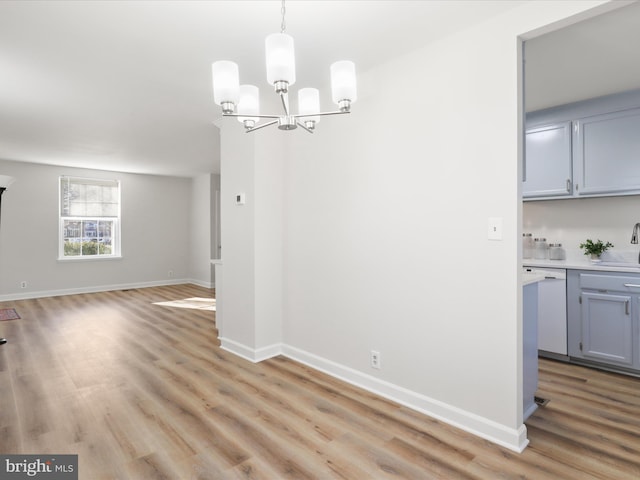 unfurnished dining area featuring a chandelier, baseboards, light wood-style floors, and a sink