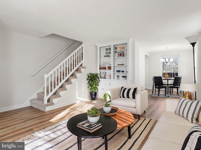 living area with stairs, a notable chandelier, wood finished floors, and baseboards