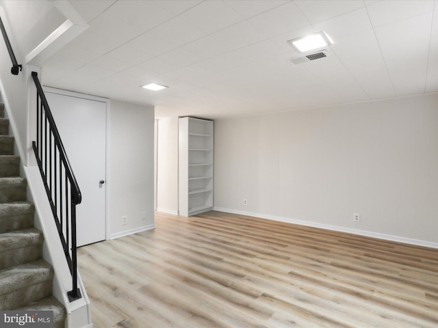 finished basement with visible vents, baseboards, light wood-style flooring, and stairs