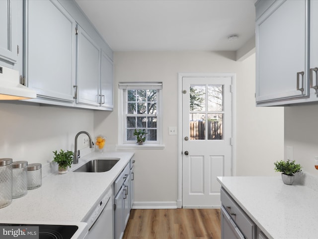 kitchen with light stone counters, range hood, wood finished floors, white dishwasher, and a sink