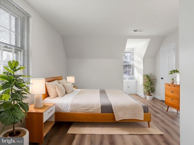 bedroom with vaulted ceiling, wood finished floors, and visible vents