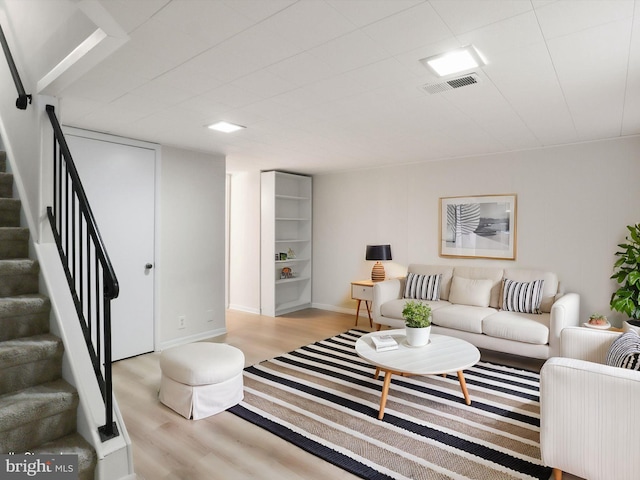 living room with visible vents, baseboards, wood finished floors, and stairs