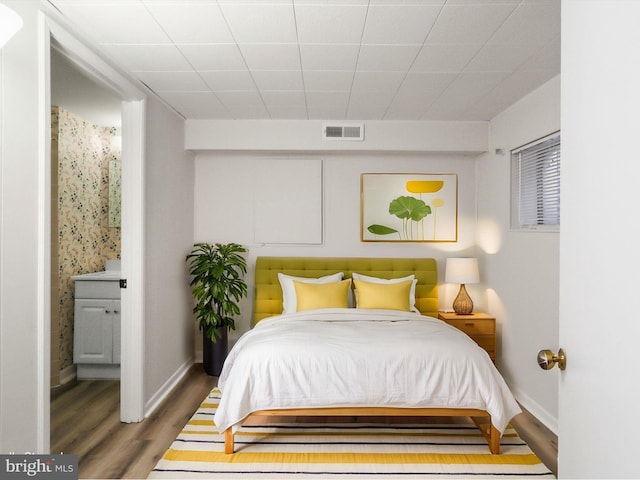 bedroom featuring connected bathroom, visible vents, baseboards, and wood finished floors