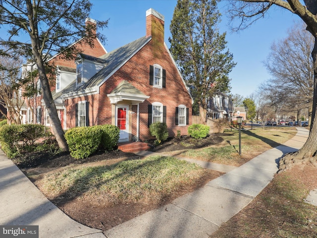 view of front of home featuring a front yard, brick siding, and a chimney