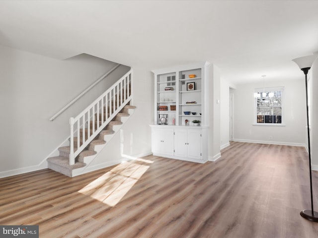 unfurnished living room featuring stairway, baseboards, and light wood finished floors