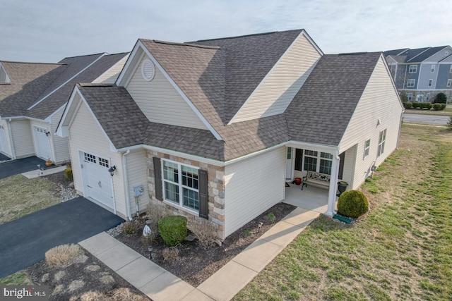 view of front of property featuring a front yard, driveway, an attached garage, a shingled roof, and stone siding