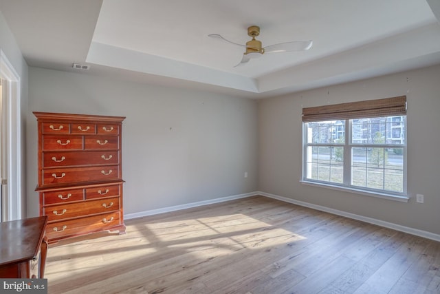 unfurnished bedroom with a tray ceiling, baseboards, visible vents, and light wood-style flooring