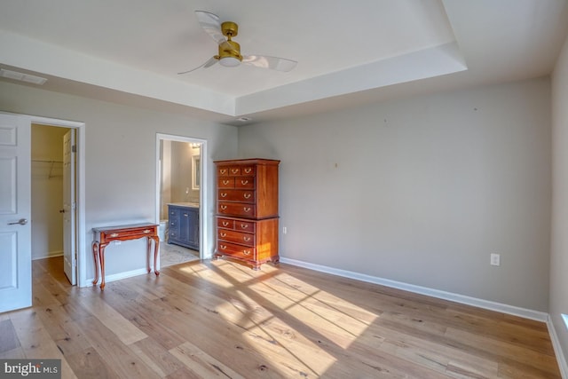 unfurnished bedroom featuring light wood finished floors, visible vents, a spacious closet, baseboards, and a tray ceiling