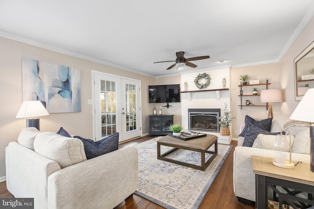 living area with crown molding, dark wood-type flooring, and a ceiling fan