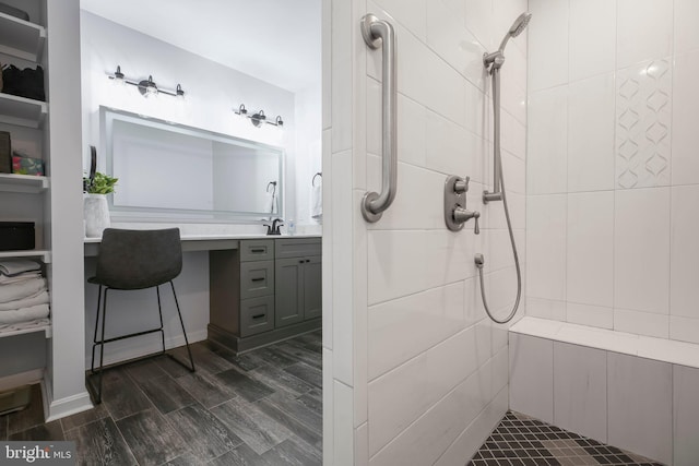 full bath featuring tiled shower, vanity, and wood finish floors