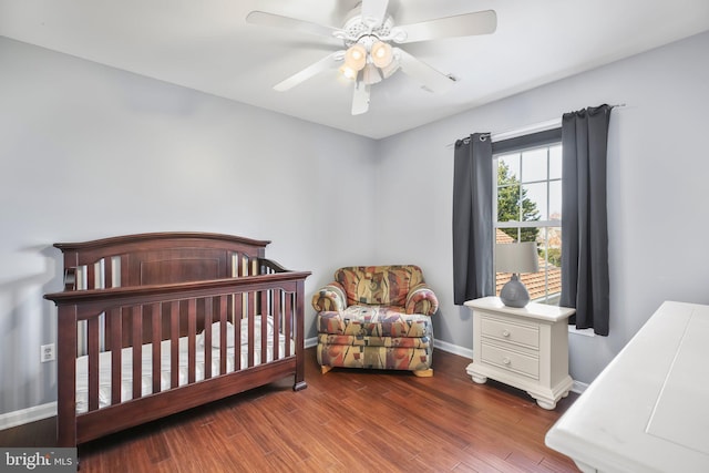 bedroom with a nursery area, ceiling fan, baseboards, and wood finished floors