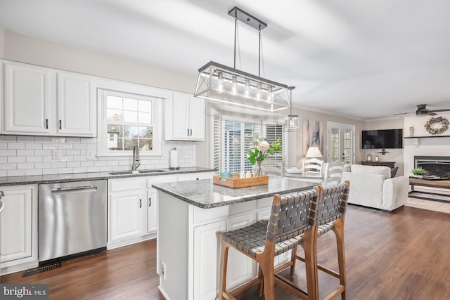 kitchen with backsplash, dark wood-style flooring, a kitchen breakfast bar, stainless steel dishwasher, and a sink