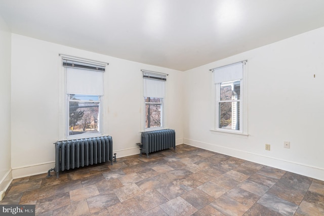 unfurnished room featuring radiator heating unit, baseboards, and stone finish flooring