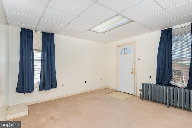 carpeted spare room with radiator, a paneled ceiling, and baseboards