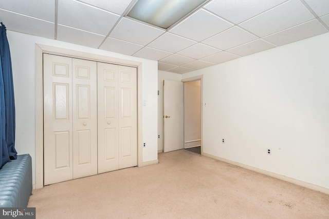 unfurnished bedroom with a drop ceiling, baseboards, carpet, and a closet