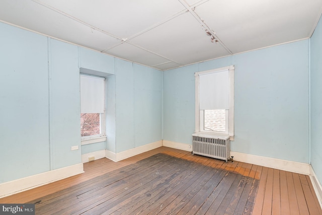 unfurnished room featuring hardwood / wood-style floors, radiator, and baseboards