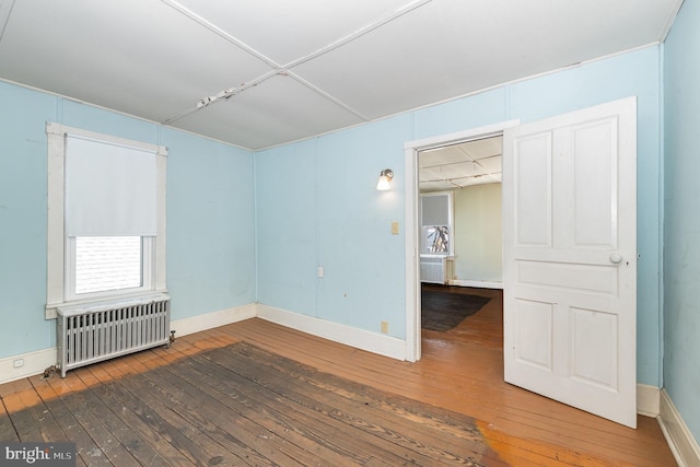 spare room featuring baseboards, radiator, and hardwood / wood-style floors