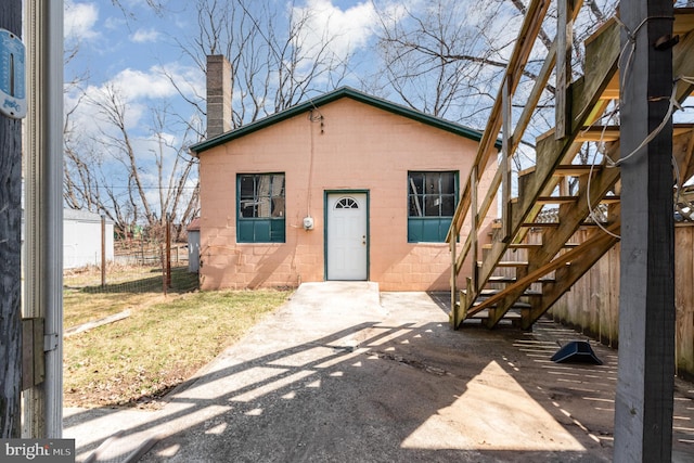 bungalow-style house with concrete block siding, a chimney, stairs, and fence