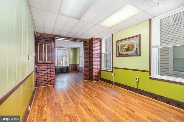 empty room featuring a paneled ceiling, radiator, wood finished floors, and brick wall