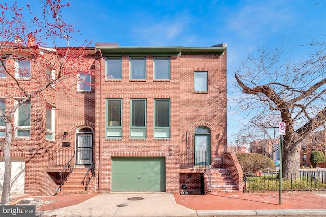 view of property featuring a garage, brick siding, driveway, and fence