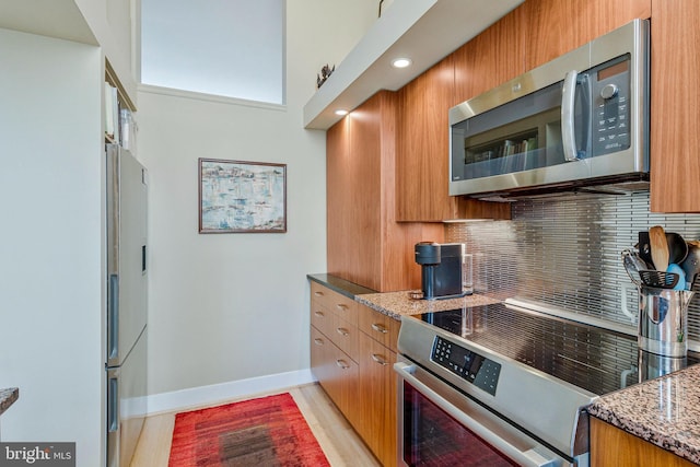 kitchen with appliances with stainless steel finishes, brown cabinetry, decorative backsplash, baseboards, and light stone countertops