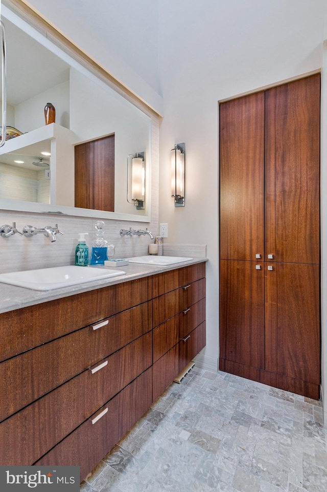 full bath featuring double vanity, backsplash, stone finish flooring, and a sink